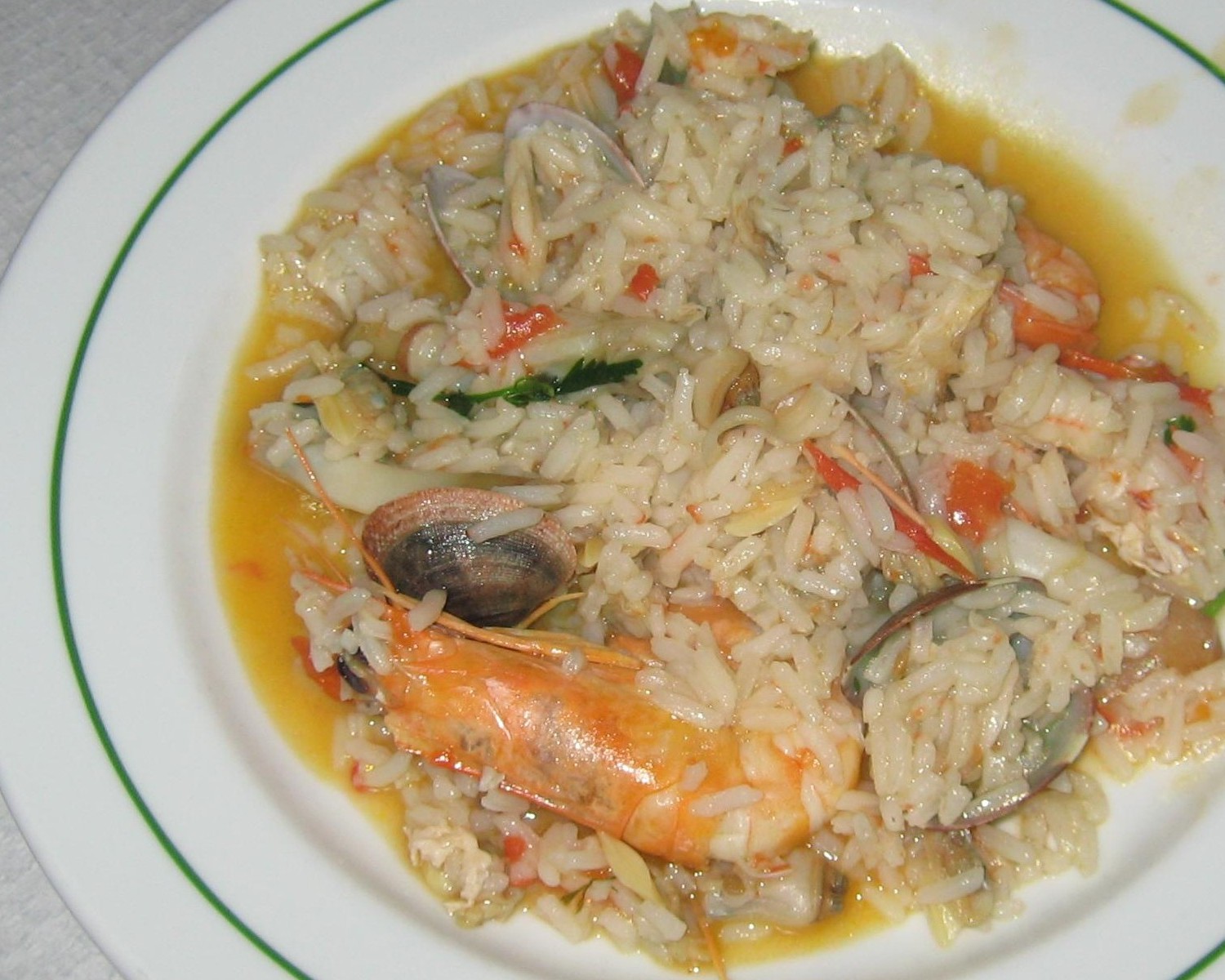 Plate of brothy seafood rice with shrimp and clams.